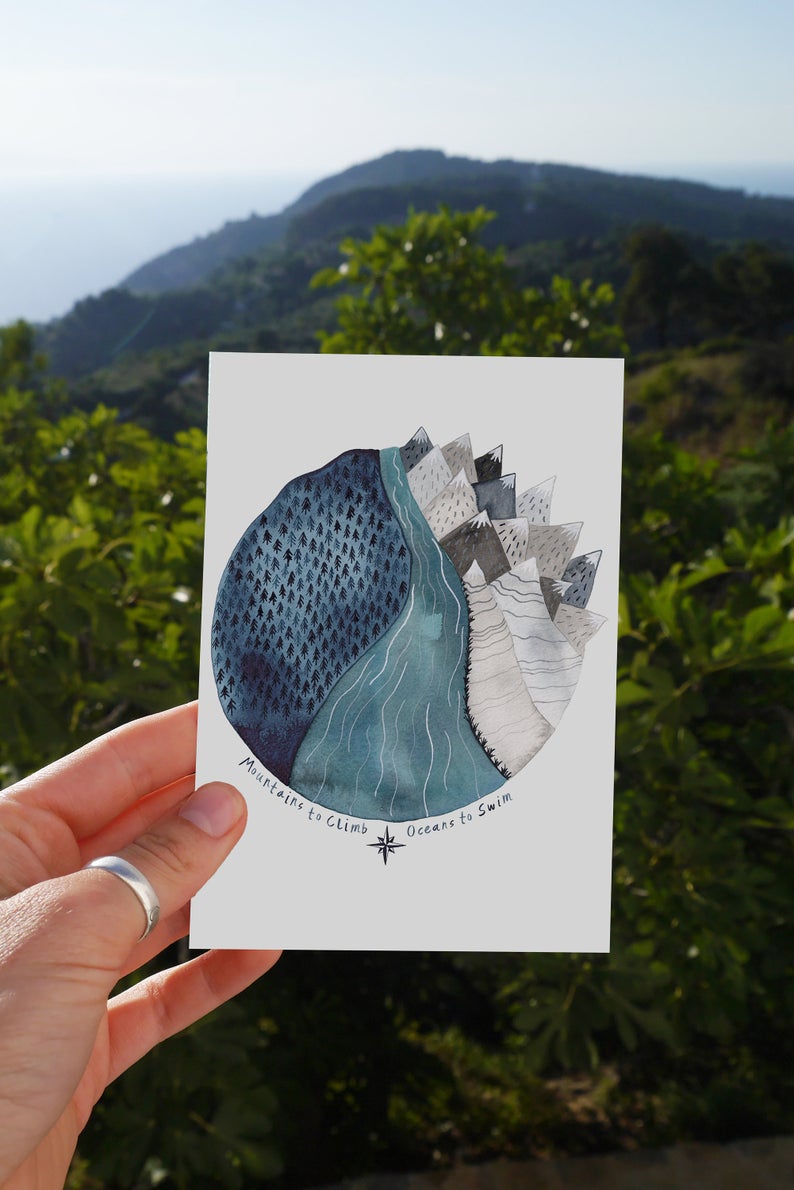 card with round blue watercolour of mountains dark sky and forest with the words ''mountains to climb oceans to swim''