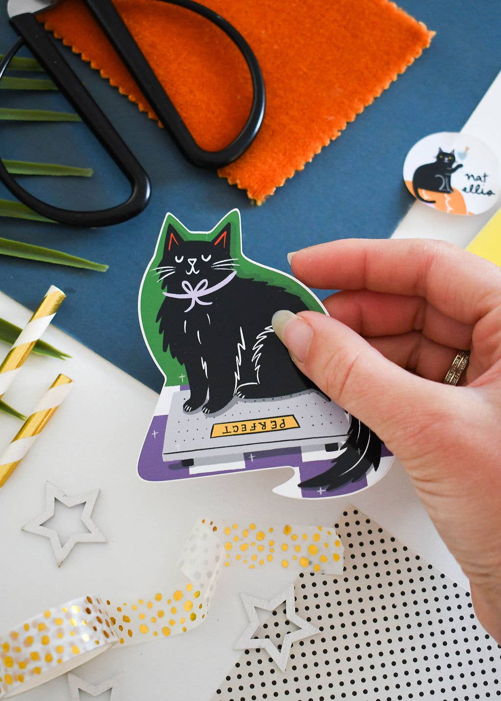 Hand holding a sticker of a cat on a craft table with scissors and fabric