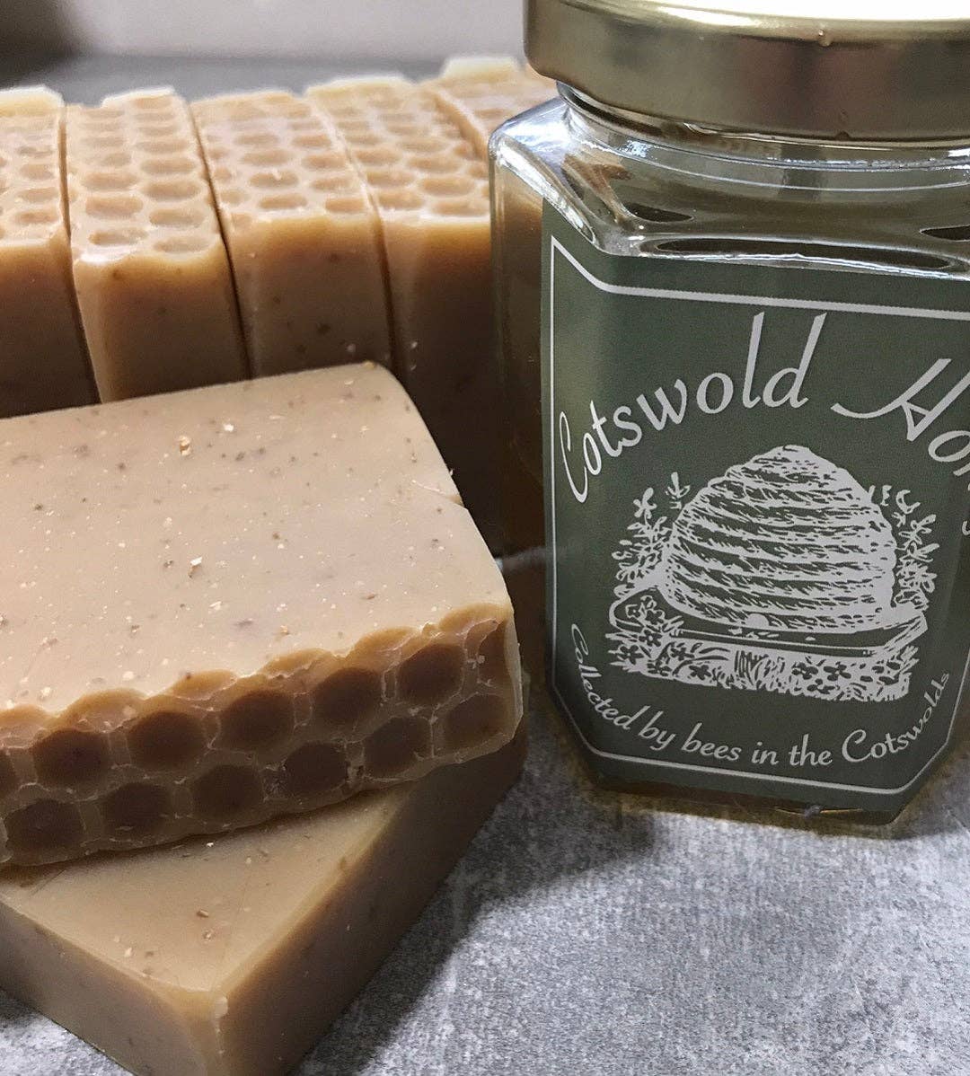 Jar of Cotswold Honey with honeycomb-patterned soap bars on a gray surface