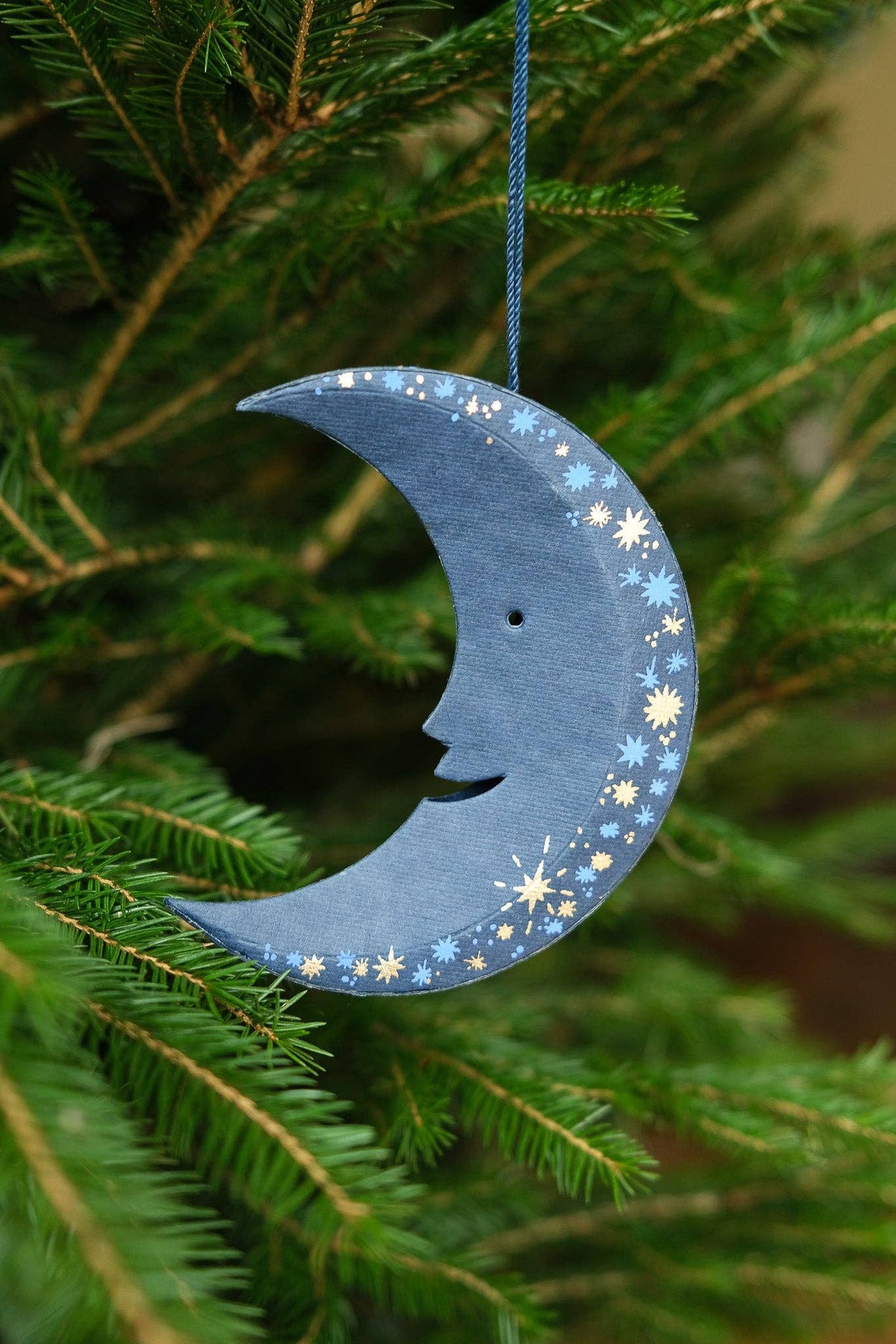 Decorative blue moon ornament with star patterns hanging on a Christmas tree.