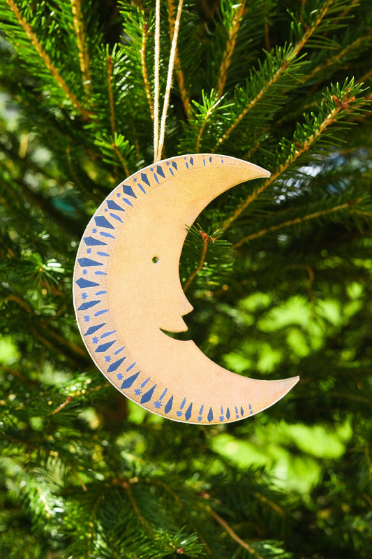 Decorative moon ornament with blue accents hanging on a Christmas tree.