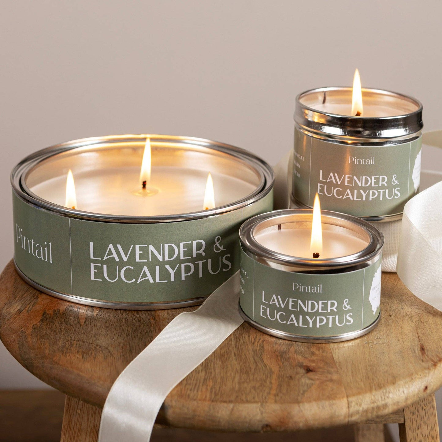 Three Pintail lavender and eucalyptus candles on a wooden surface with a white ribbon.