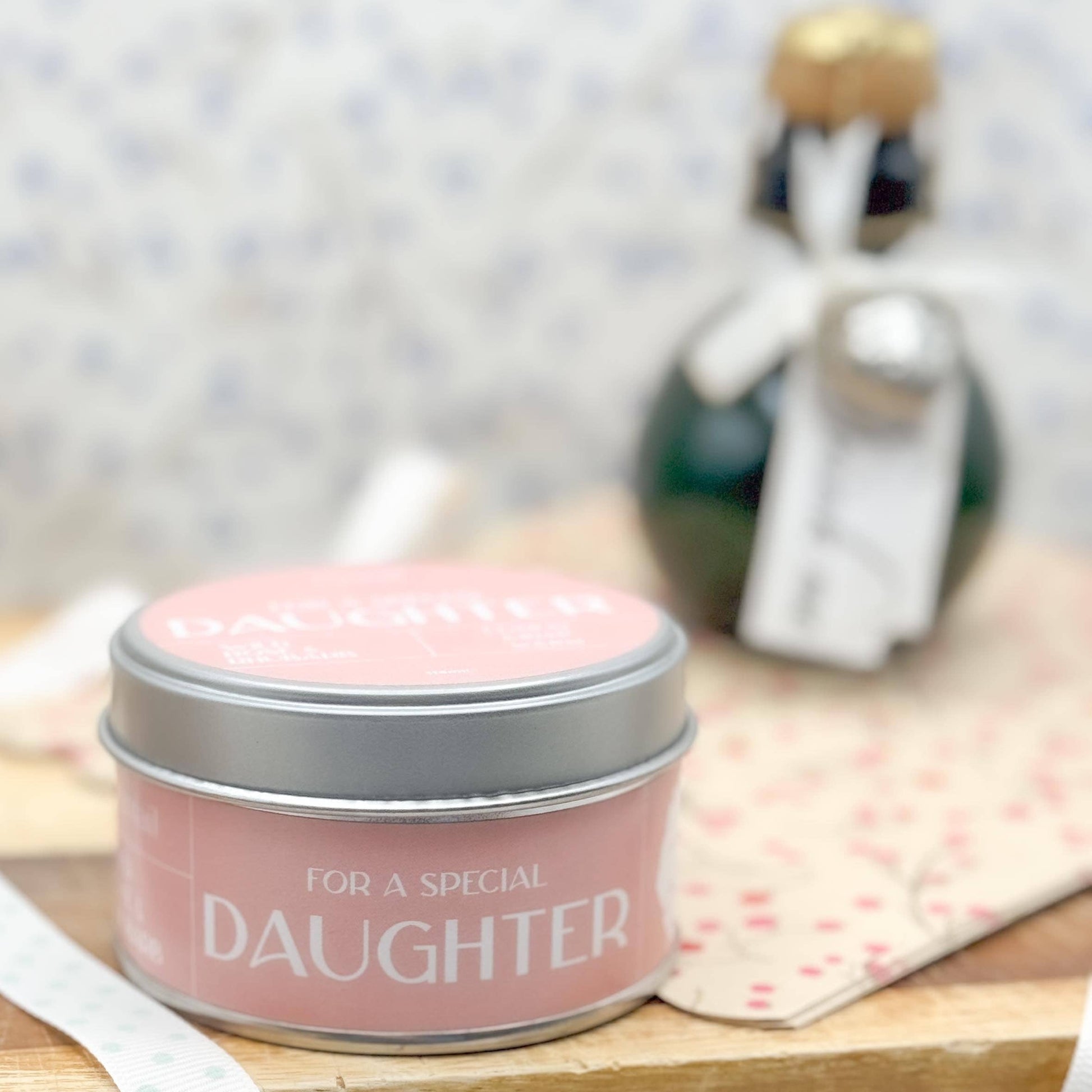 Pink candle in a tin labeled 'For a Special Daughter' on a wooden surface with a blurred background.