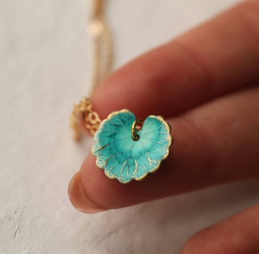 Turquoise flower-shaped pendant with gold accents held by a hand against a neutral background