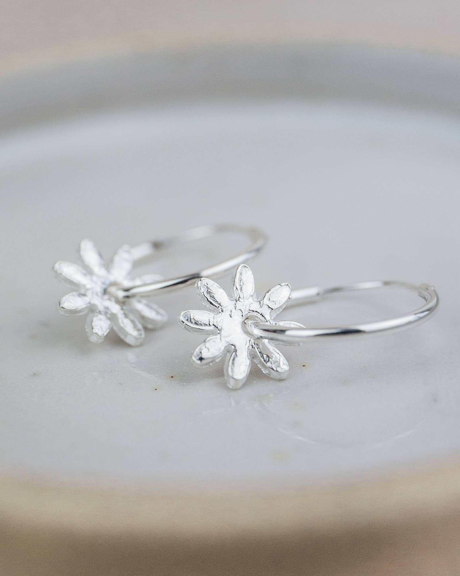 Silver flower-shaped hoop earrings on a light gray surface