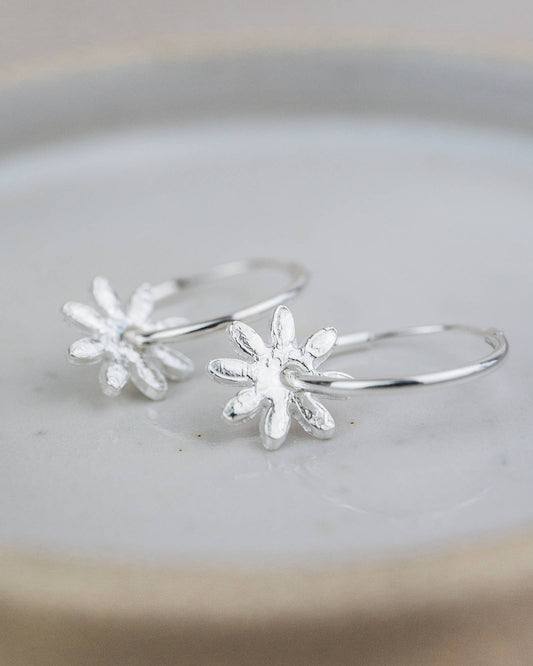 Silver flower-shaped hoop earrings on a light gray surface