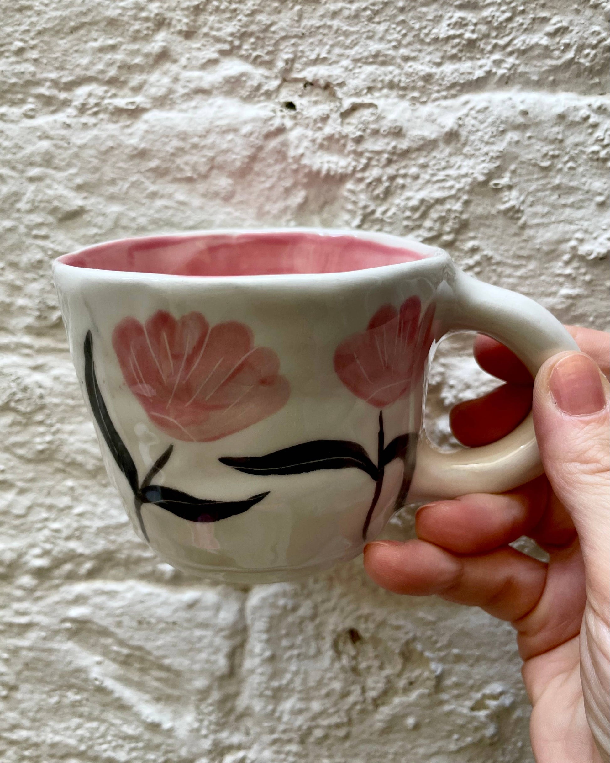 Hand holding a mug with floral design against a textured wall.