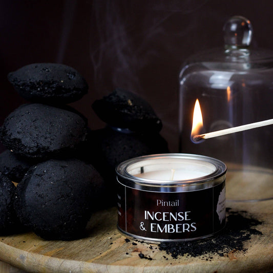 Candle labeled 'Incense & Embers' with smoking stones and a match on a dark background
