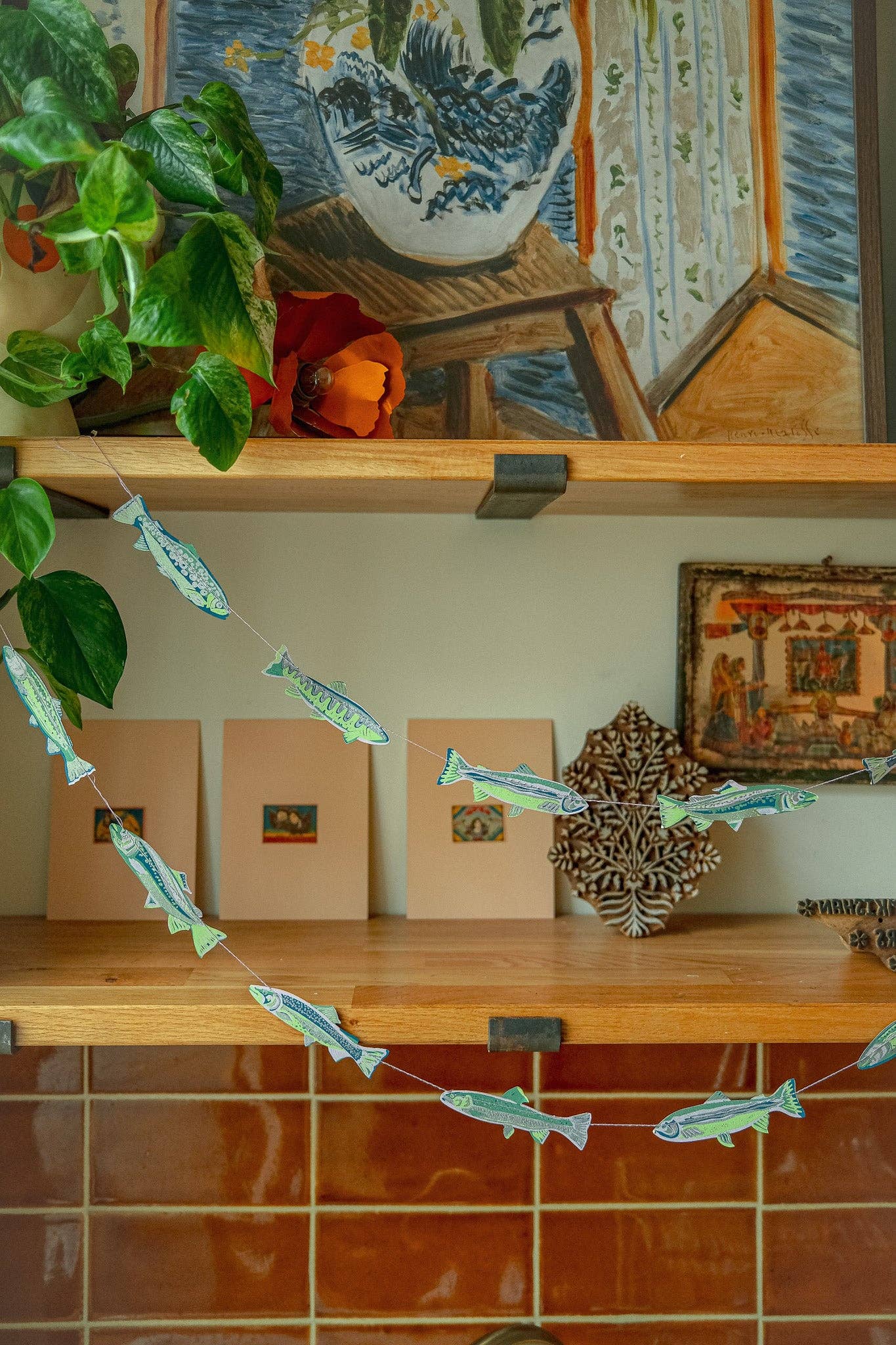 Decorative shelf with plants, books, and a fish-themed string decoration.