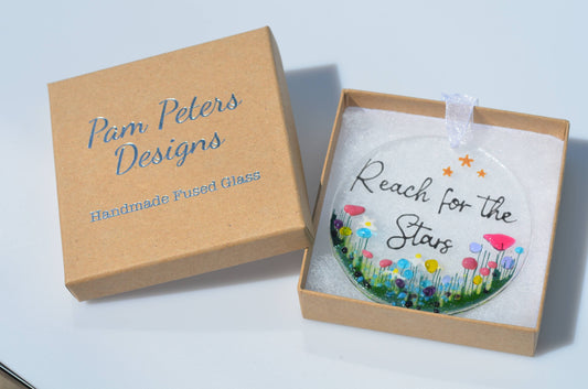 Decorative glass ornament with 'Reach for the Stars' text in a 'Pam Peters Designs' box.