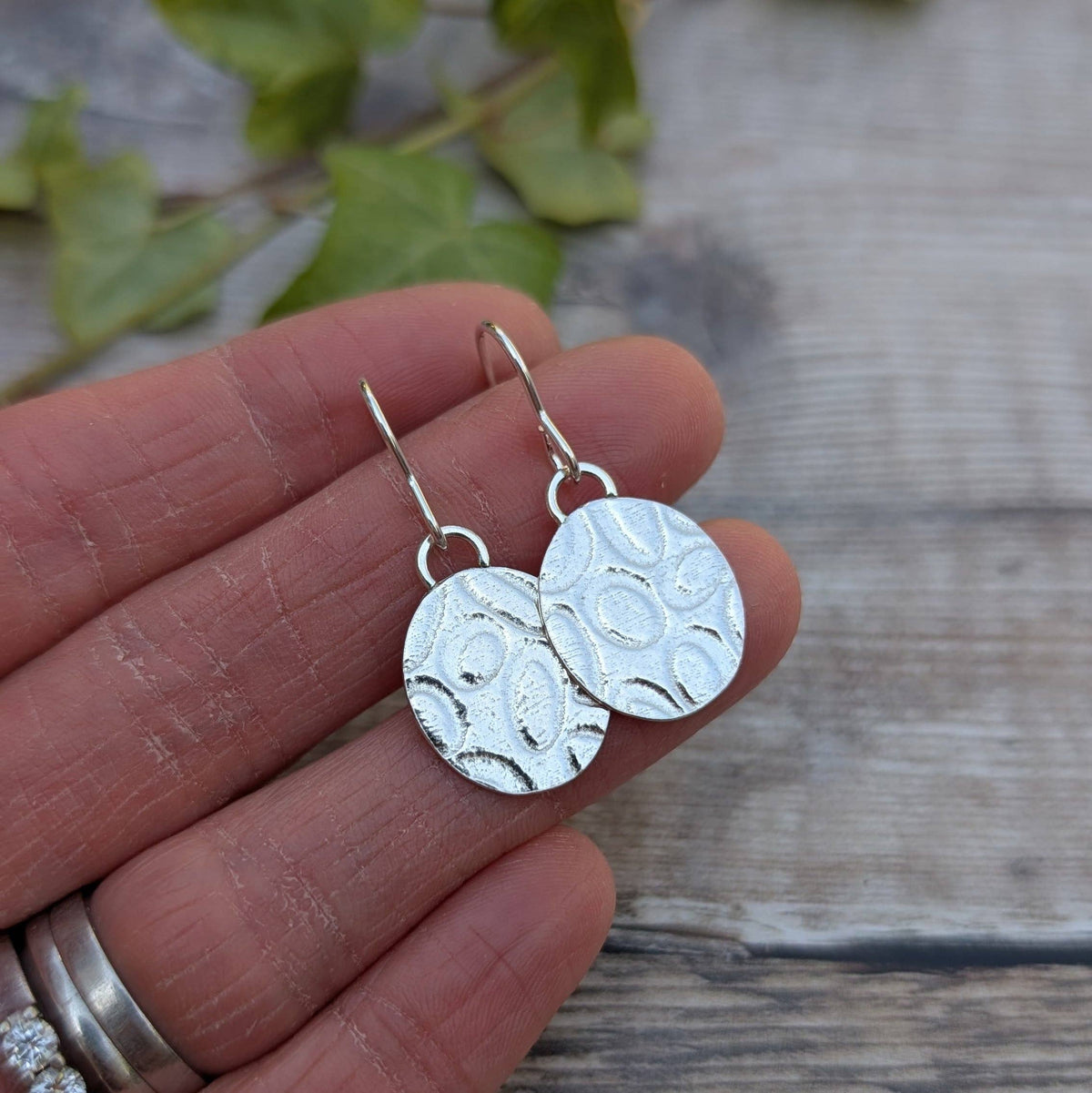 Silver earrings held between fingers with a natural background
