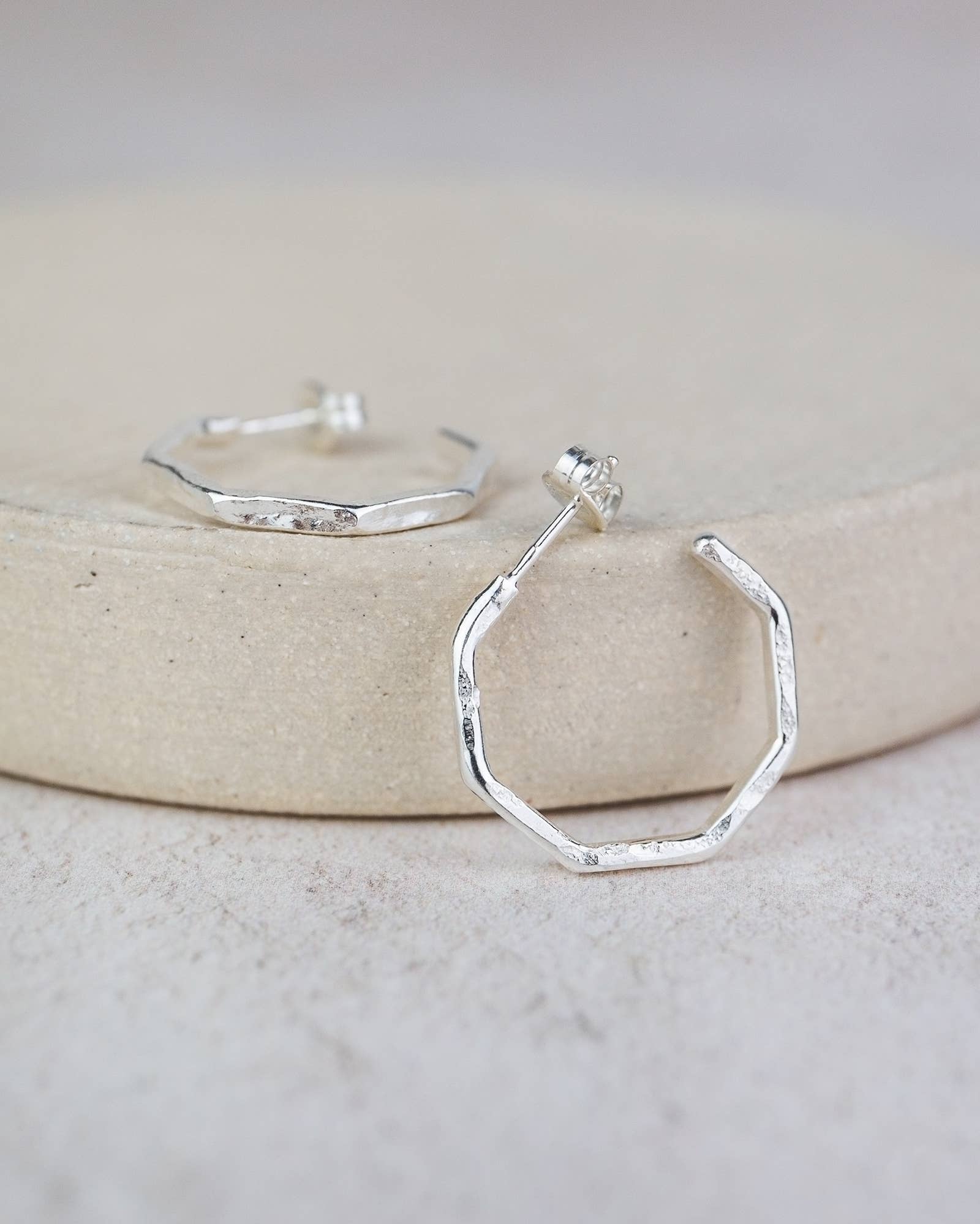Hexagonal silver hoop earrings on a light background