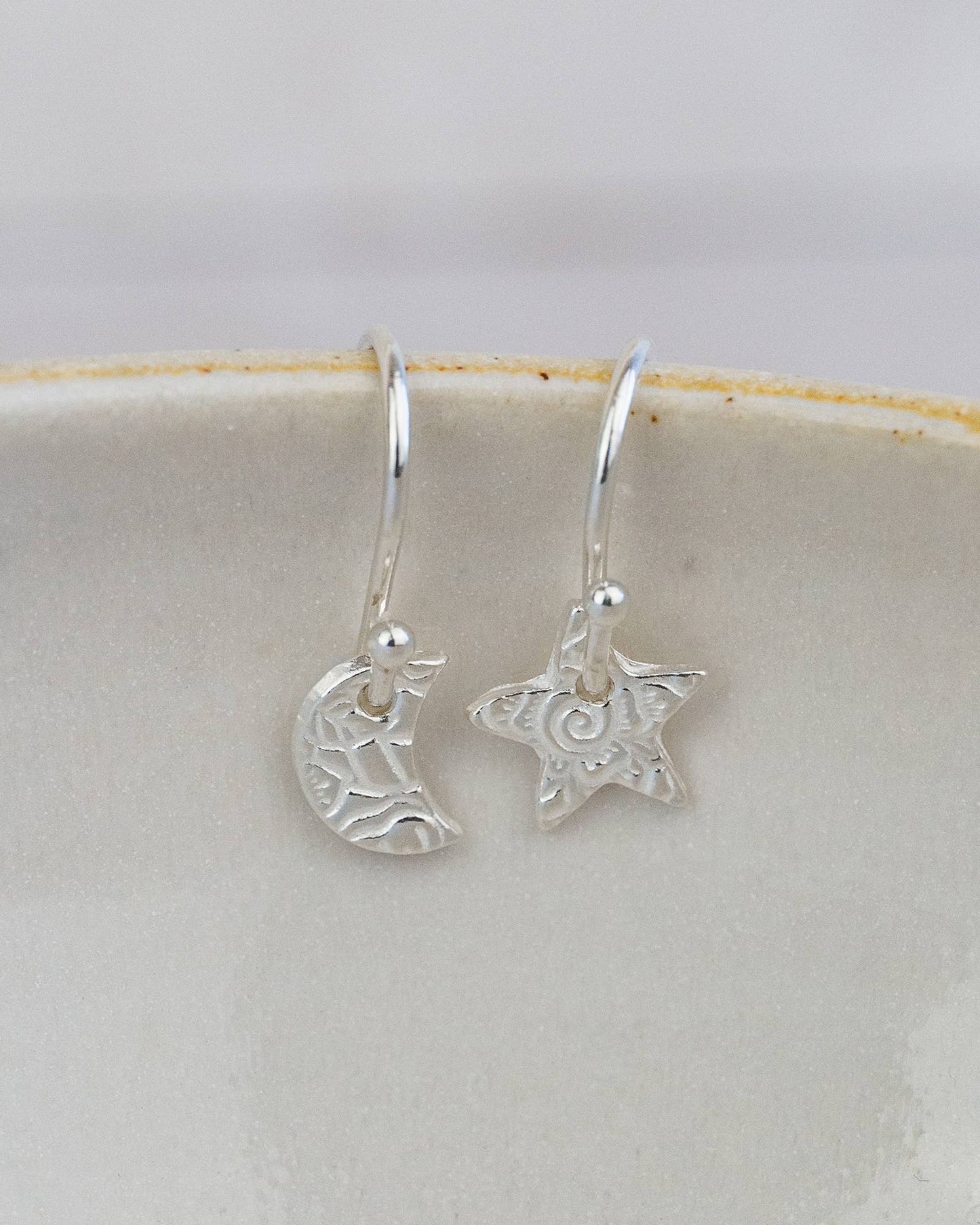 Silver earrings with star and moon designs on a white background