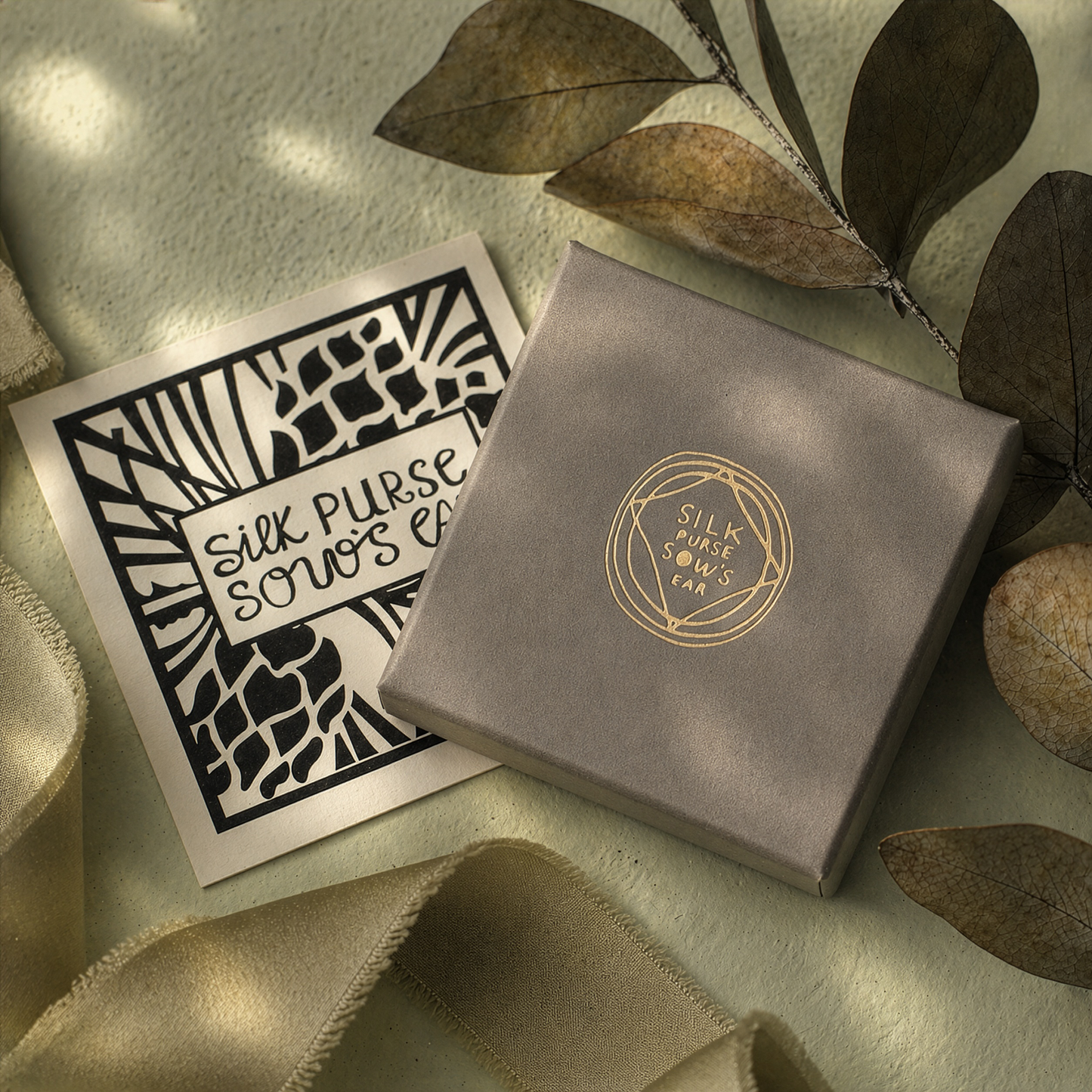 Silk Purse Sows Ear packaging with a card on a textured surface with leaves.