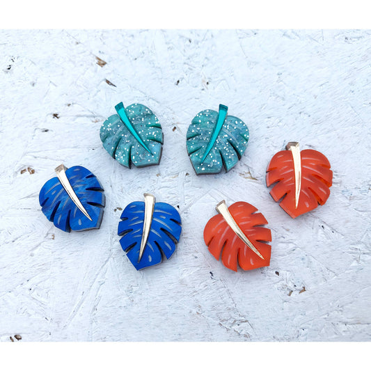 Colorful leaf-shaped earrings on a textured white surface