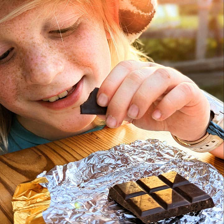 Child eating a chocolate bar outdoors with sunlight
