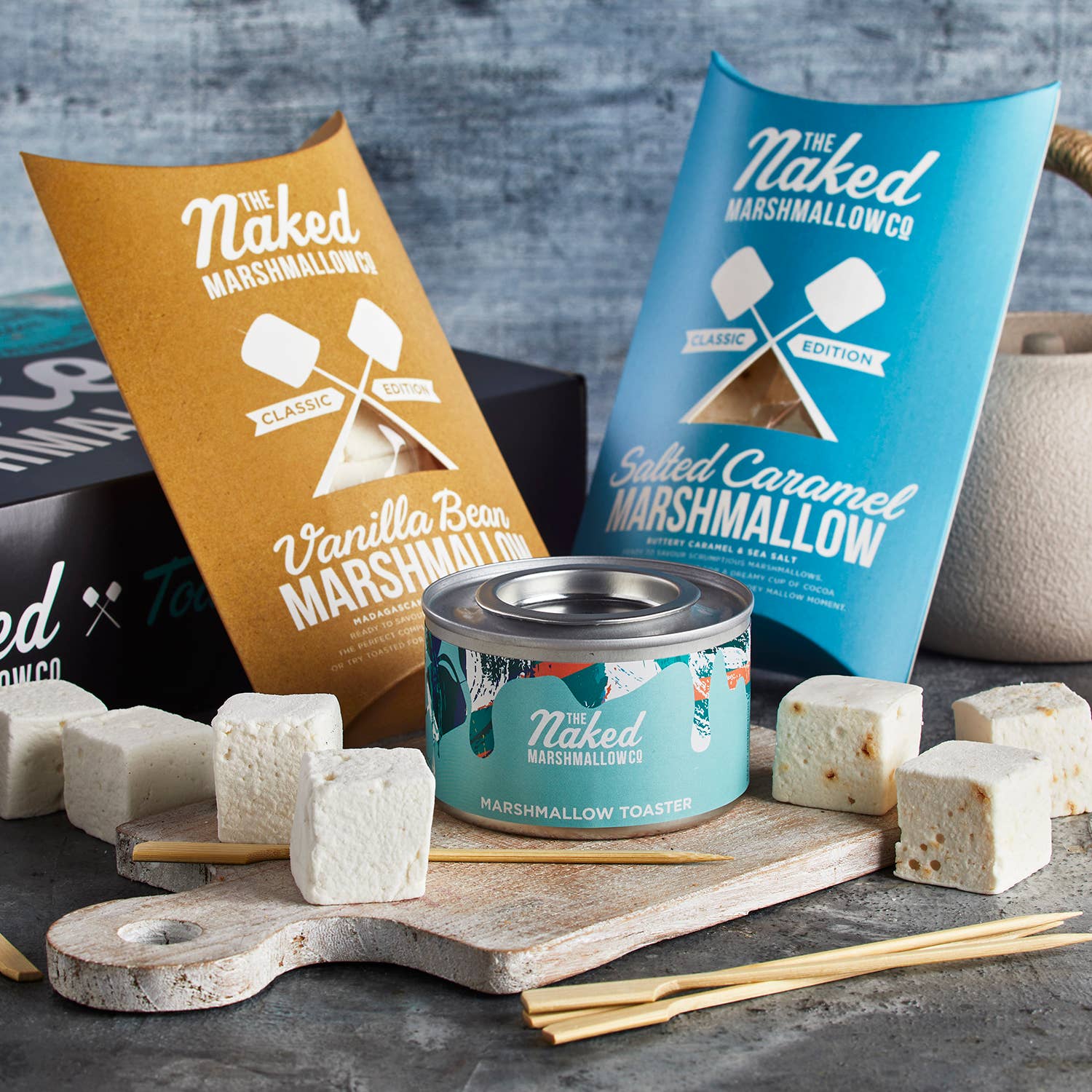 Naked Marshmallowco products including marshmallows, packaging, and a toaster on a gray surface.
