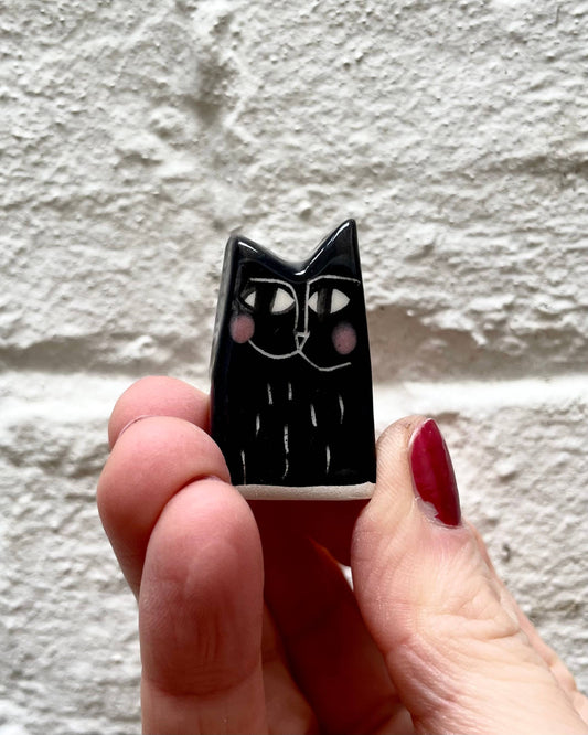 Black cat-shaped object held by a hand against a textured white background