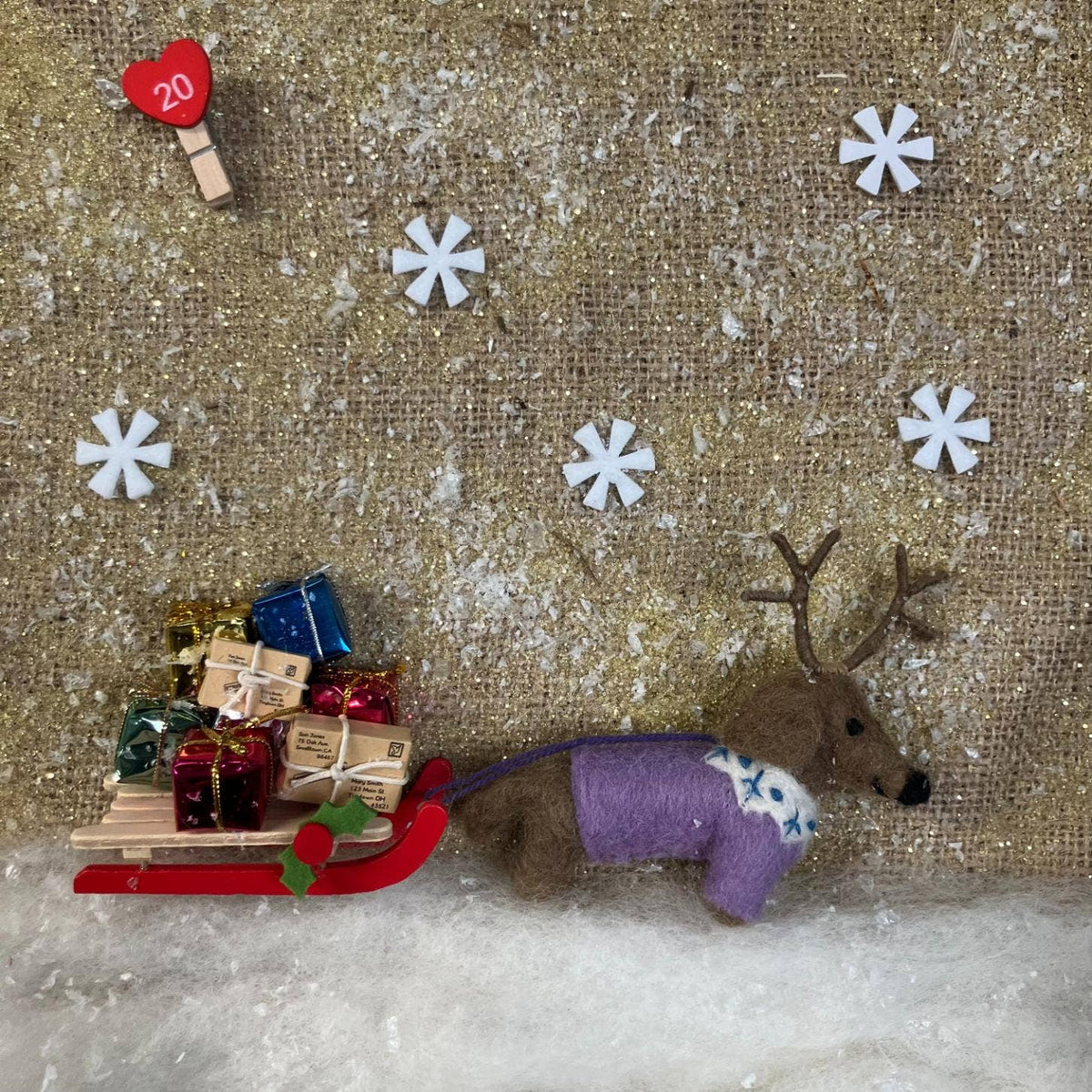 Small reindeer with a sleigh full of presents on a textured gold background with snowflakes.