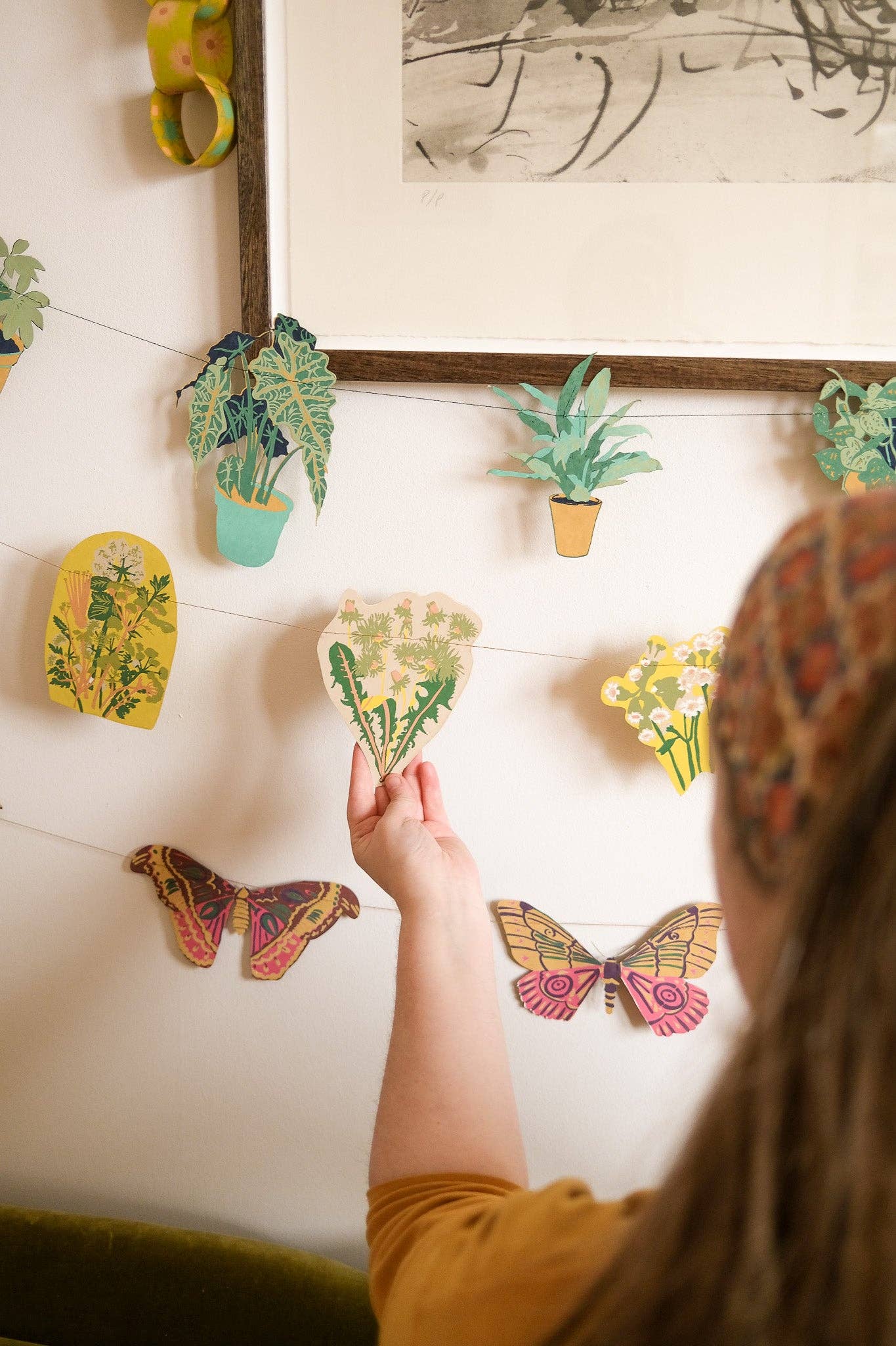 Person arranging decorative paper plants and butterflies on a wall.