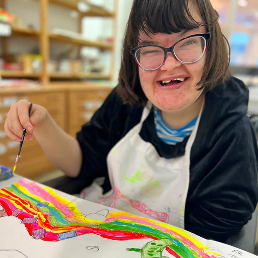 Person with glasses and an apron, engaged in a creative activity with colorful artwork.