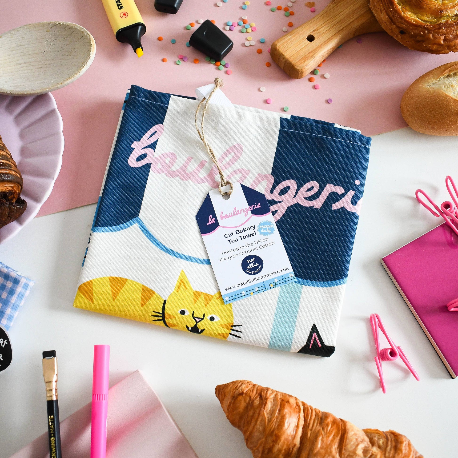 Culinary-themed kitchen towel with cat design on a table with pastries and utensils.