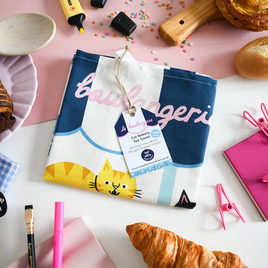 Culinary-themed kitchen towel with cat design on a table with pastries and utensils.