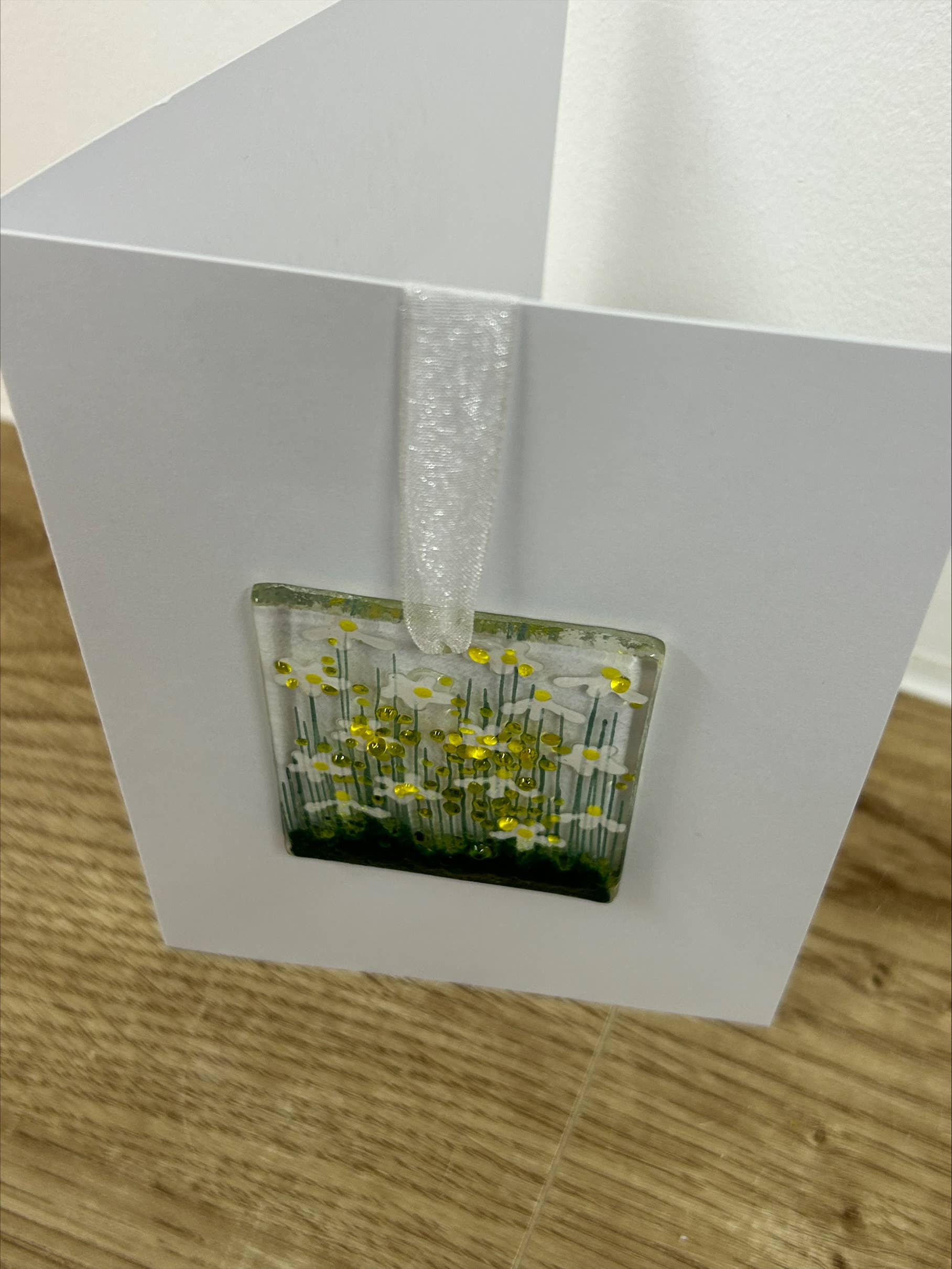 White card with a clear window displaying a small glass block with floral design on a wooden surface.