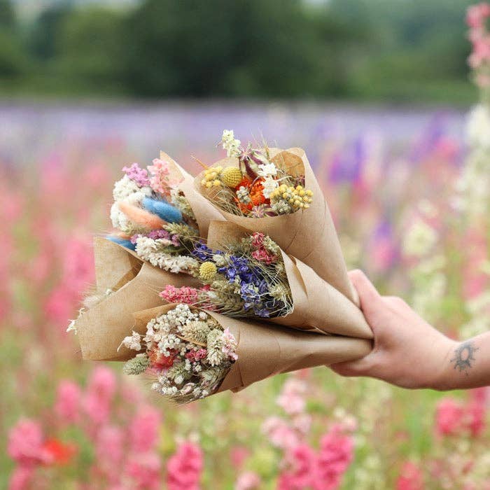 Bouquet of flowers wrapped in brown paper held against a blurred flower field background
