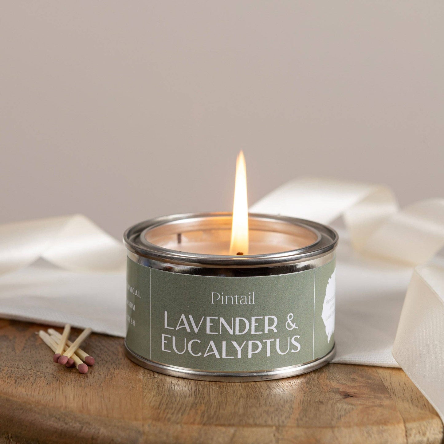 Candle in a tin labeled 'Lavender & Eucalyptus' by Pintail, with matches on a wooden surface.