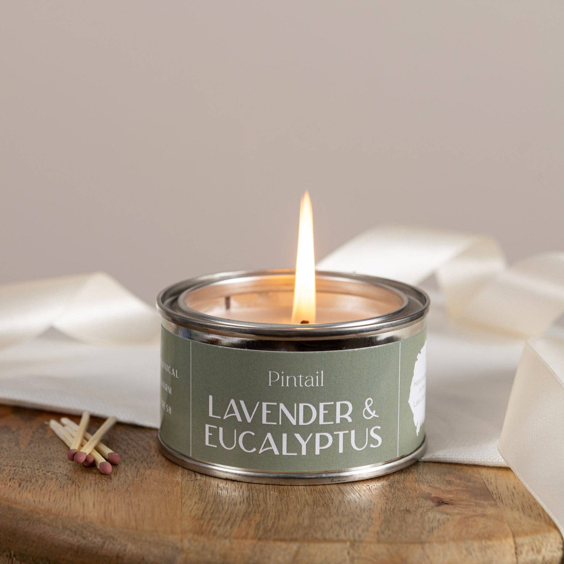 Candle in a tin labeled 'Lavender & Eucalyptus' by Pintail, with matches on a wooden surface.