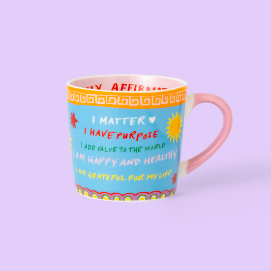 Colorful mug with motivational phrases on a light purple background
