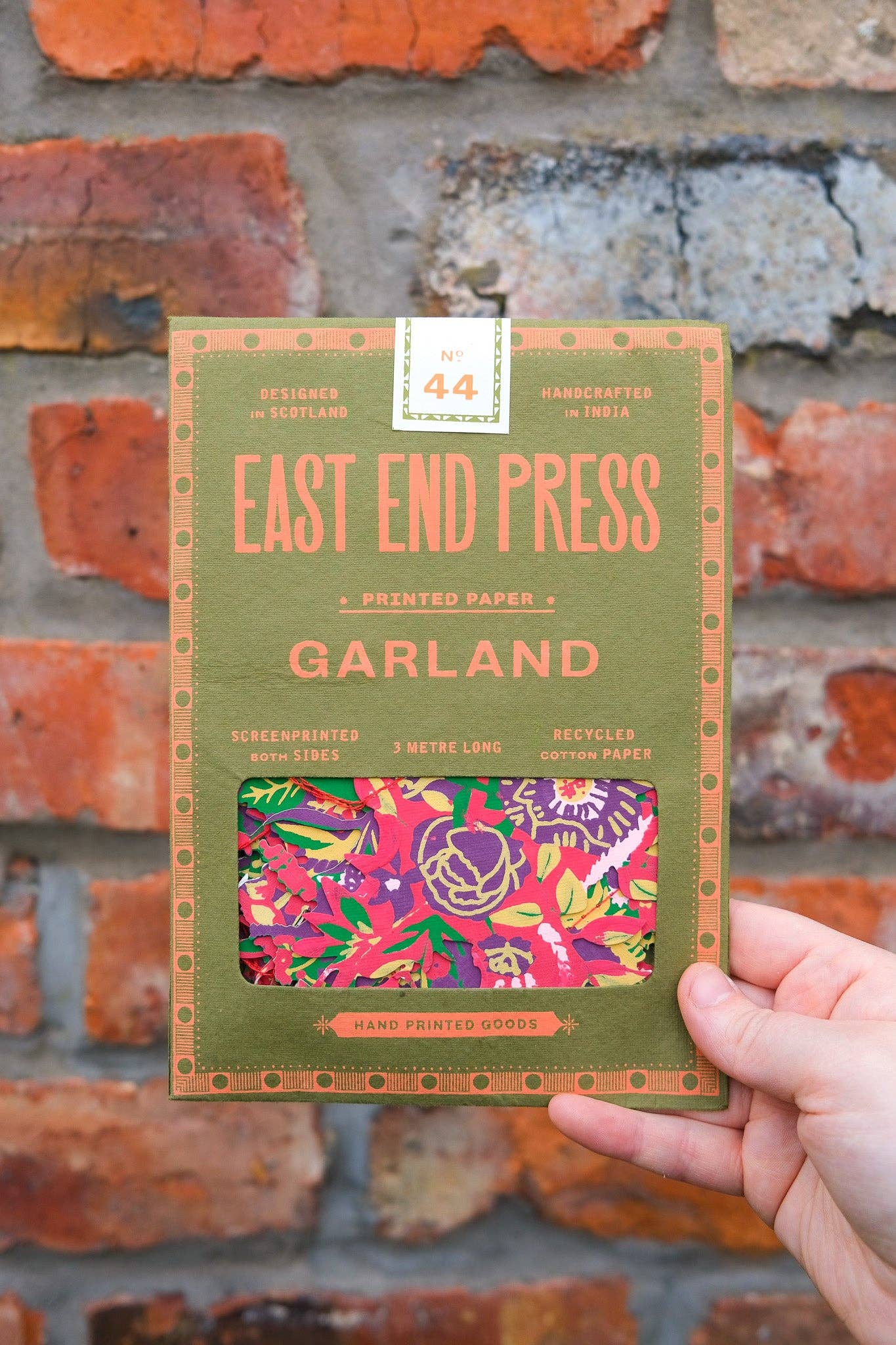 Handheld package of 'Garland' by East End Press against a brick wall background