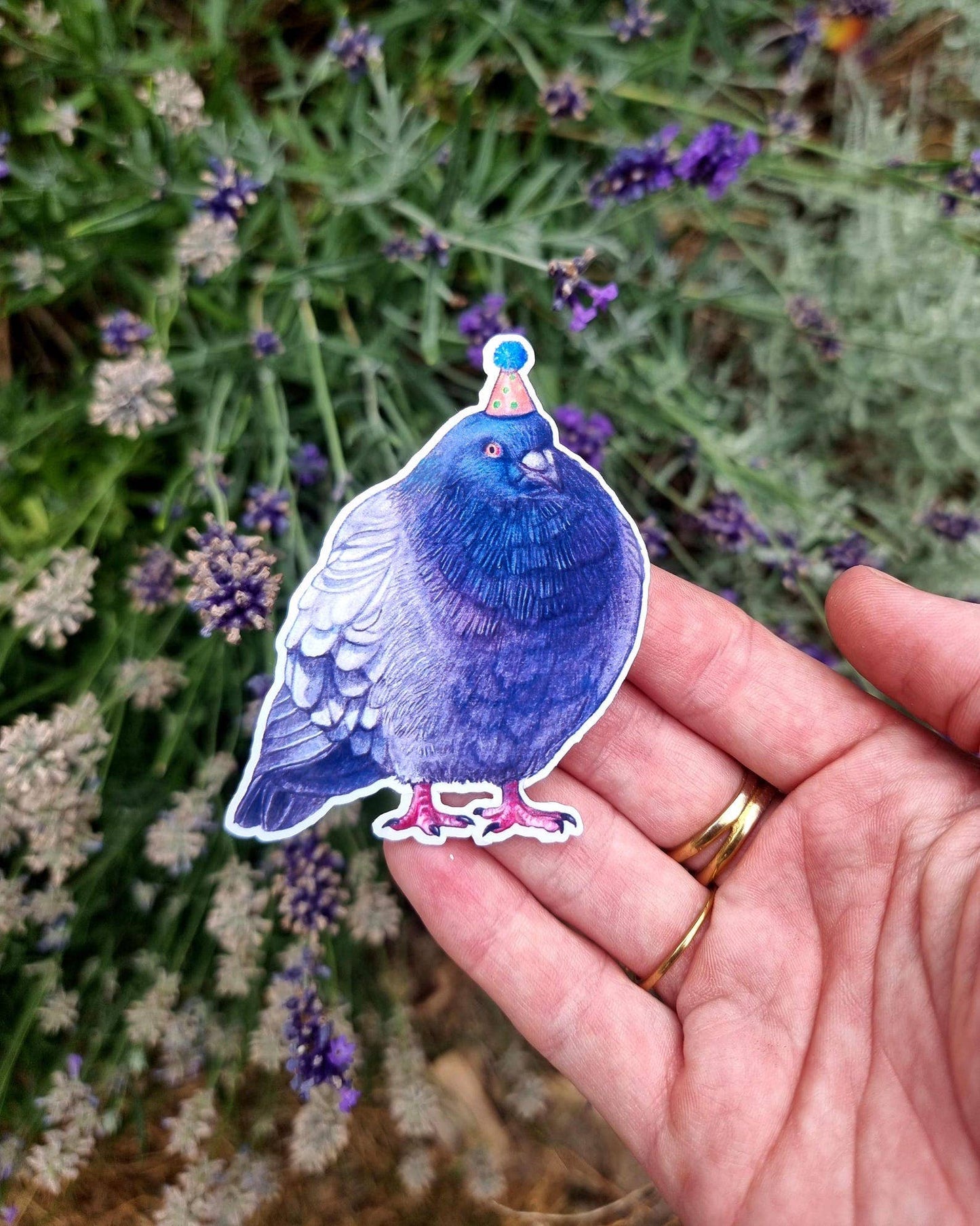 Blue pigeon sticker held in a hand with lavender flowers in the background