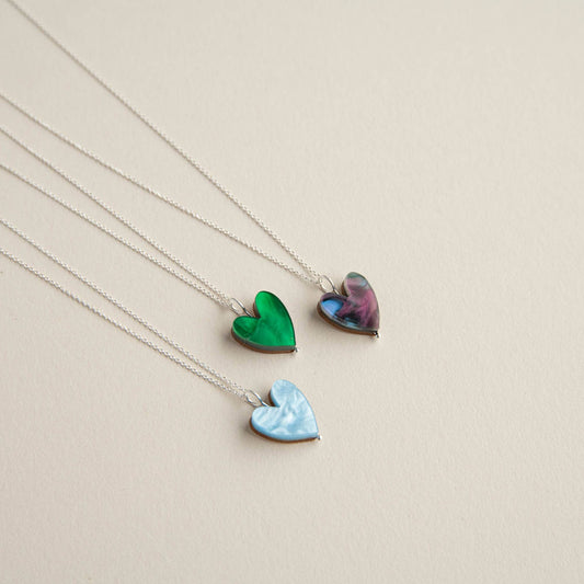 Three heart-shaped pendants on silver chains against a beige background