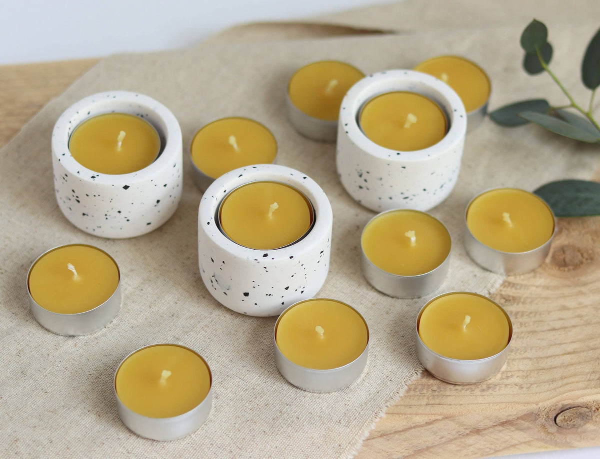 Yellow candles in white ceramic holders on a wooden surface with a beige cloth background