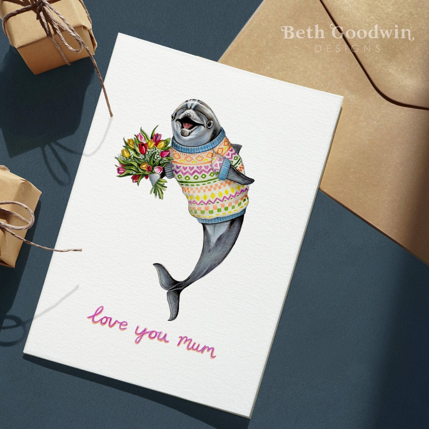 Card with a dolphin wearing a sweater and holding flowers, with 'love you Mum' text, on a dark surface.