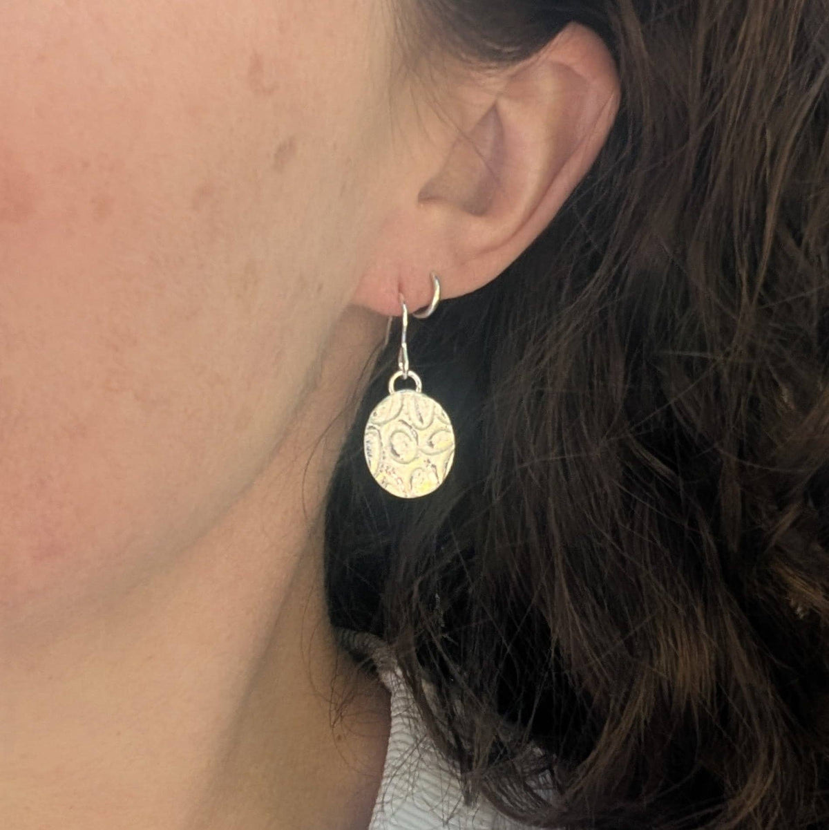 Close-up of a person wearing gold earrings with intricate designs.