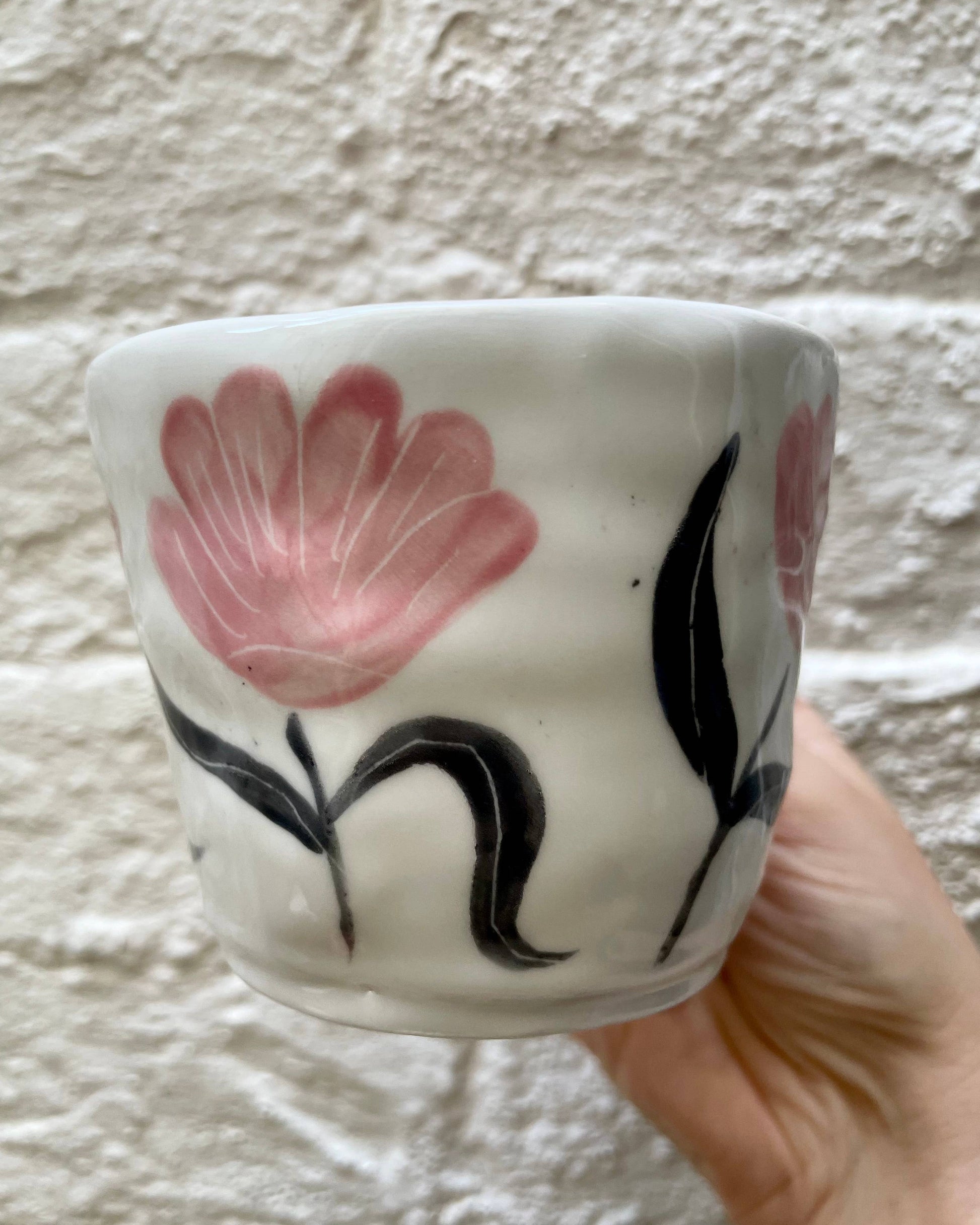 Ceramic cup with floral design held against a textured wall.