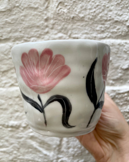 Ceramic cup with floral design held against a textured wall.