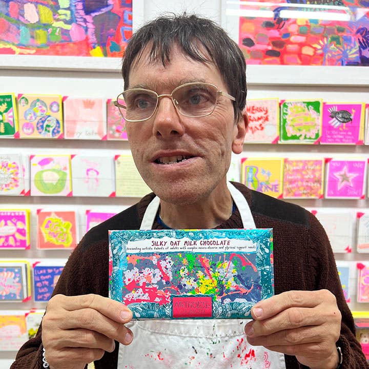 Person holding a colorful chocolate bar in front of a display of greeting cards