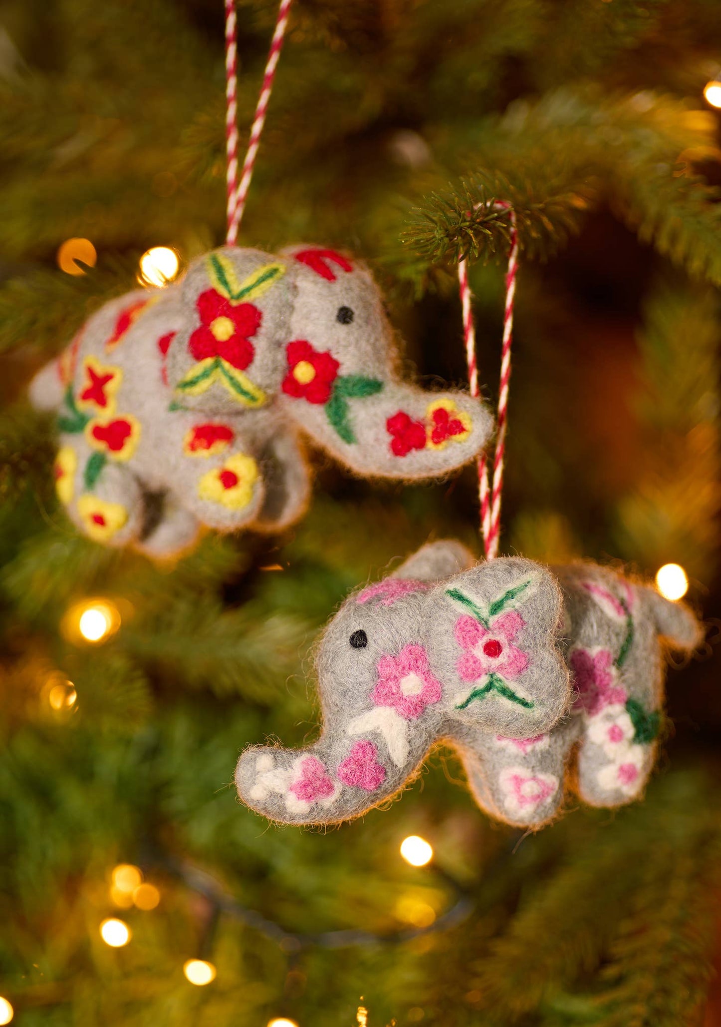 Two embroidered felt elephant decorations with red and white hanging cords, featuring colorful floral patterns.
