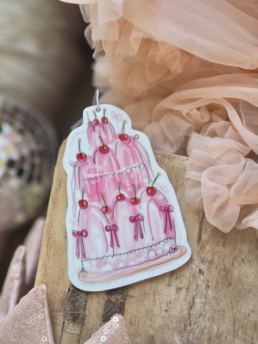 Sticker of a pink cake with cherries on a wooden surface