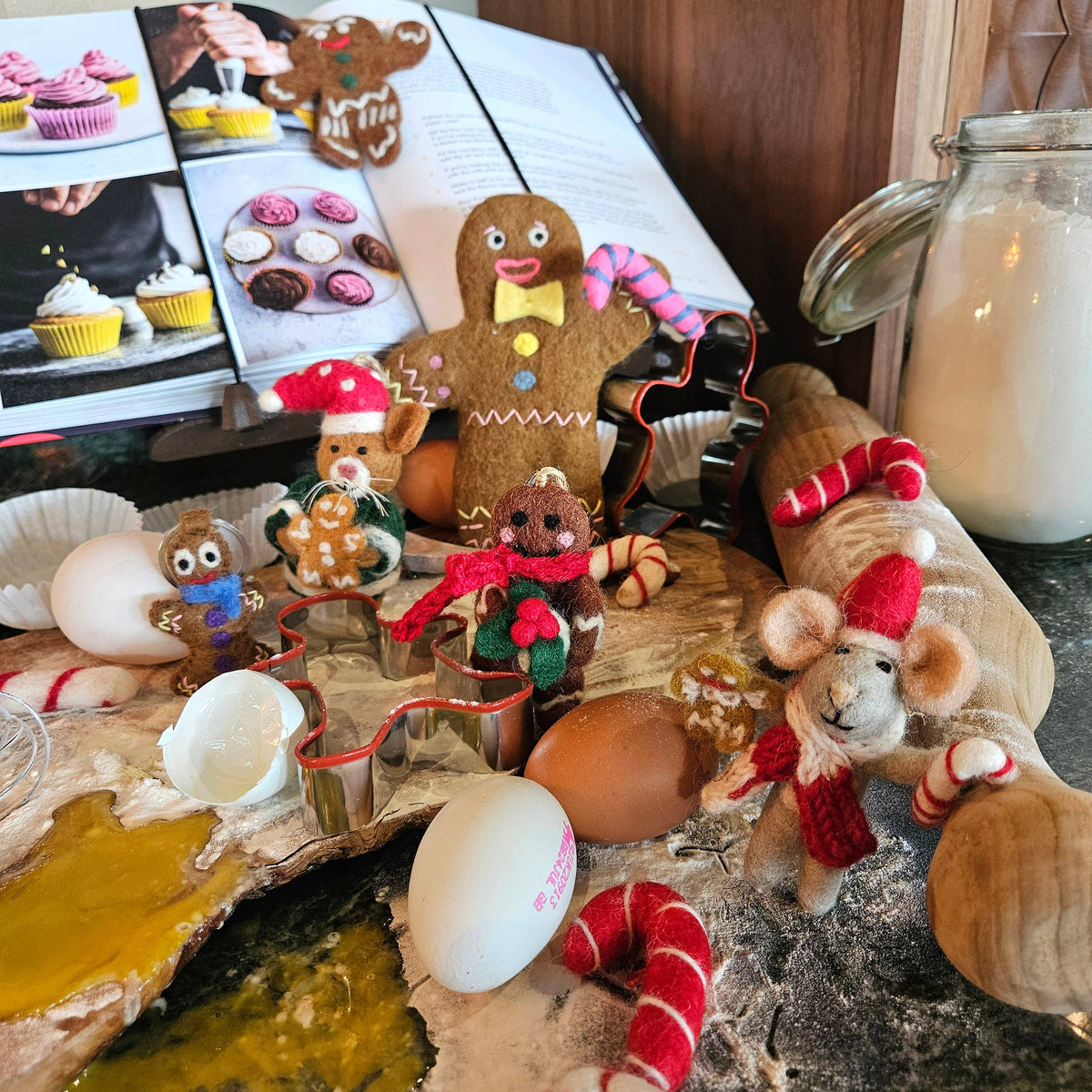 Decorative gingerbread figures and mice on a rustic surface with a cookbook in the background.