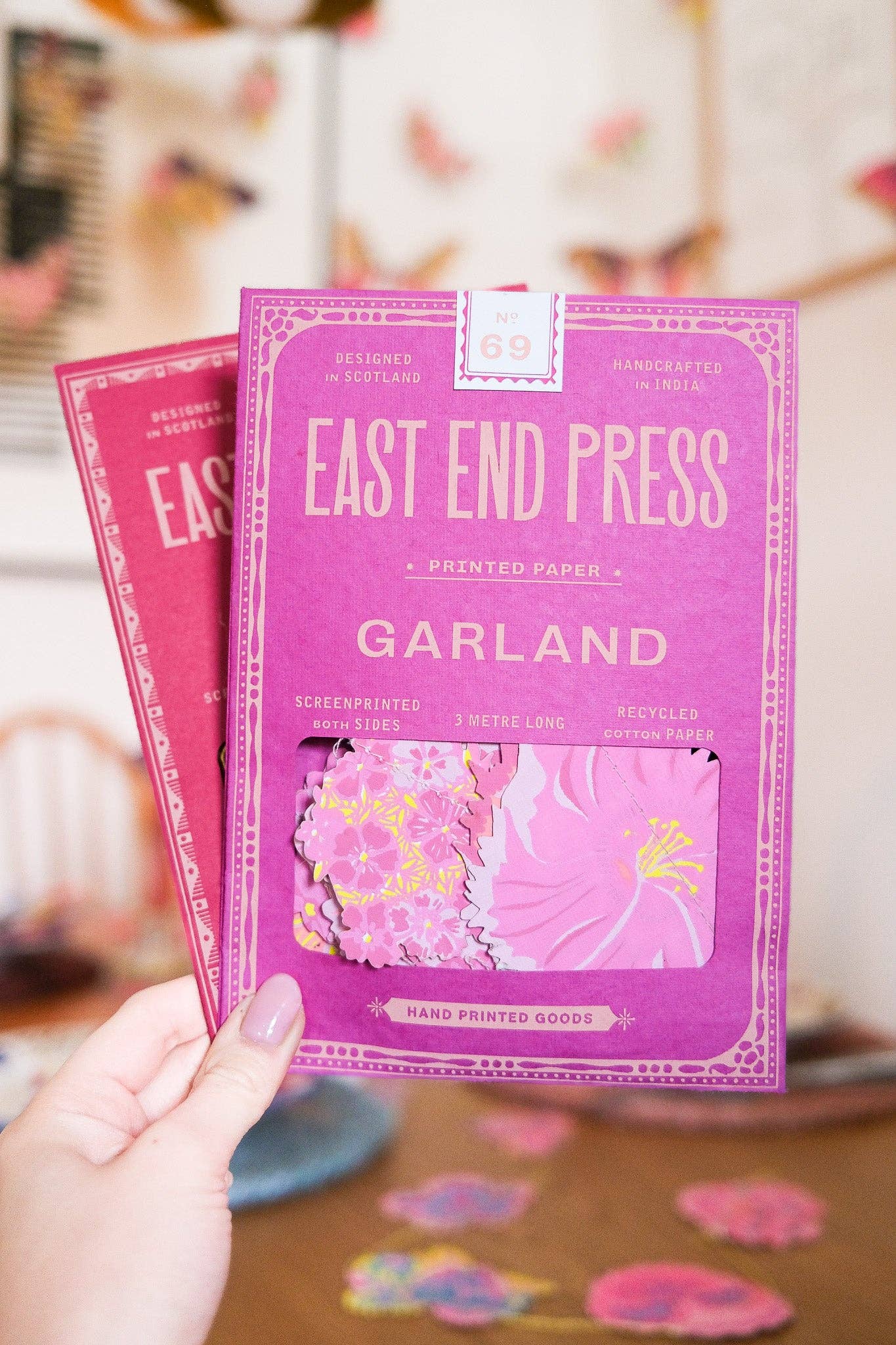Purple 'East End Press Garland' product packaging held by a hand with pink nail polish.