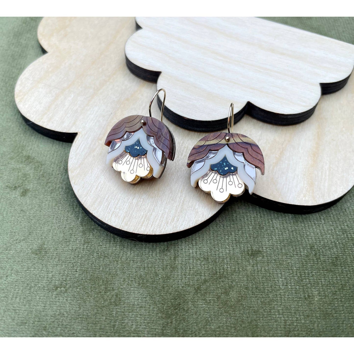 Pair of earrings with decorative design on a wooden stand against a green background