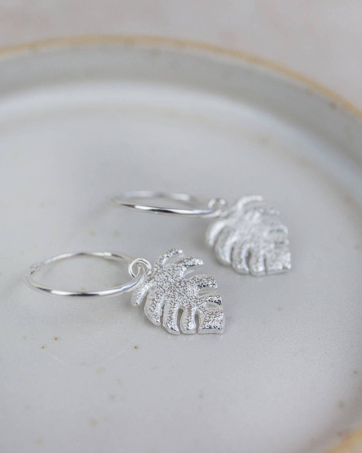 Silver hoop earrings with leaf-shaped charms on a light background