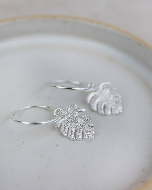 Silver hoop earrings with leaf-shaped charms on a light background