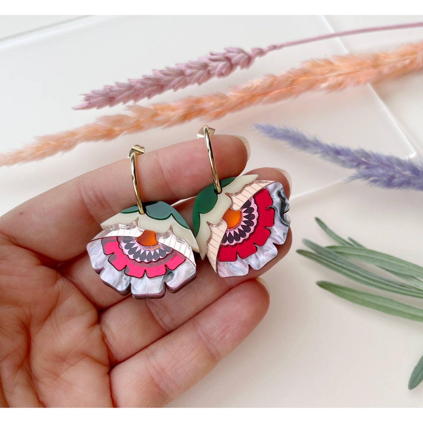 Colorful floral earrings held in a hand with a soft background