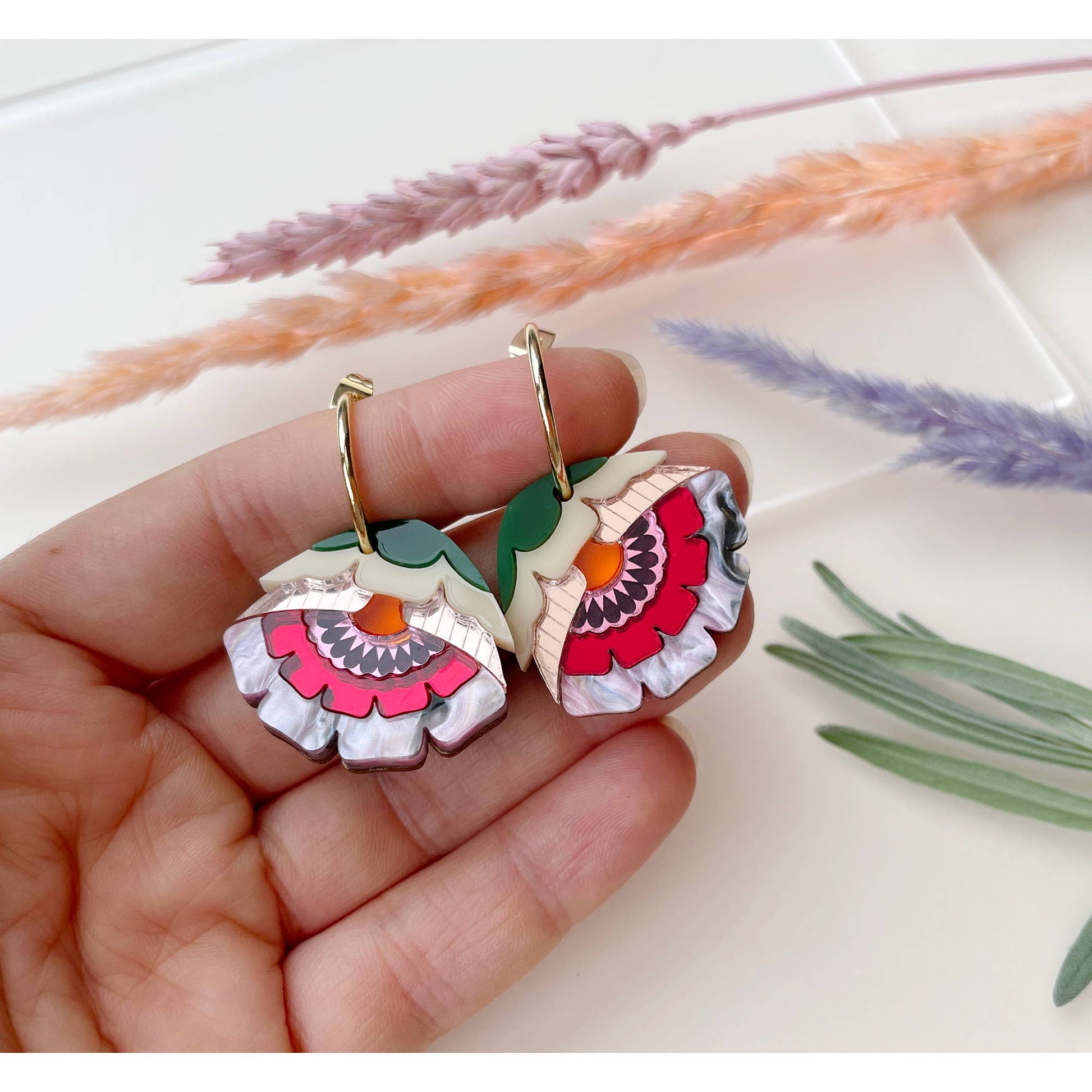 Colorful floral earrings held in a hand with a soft background